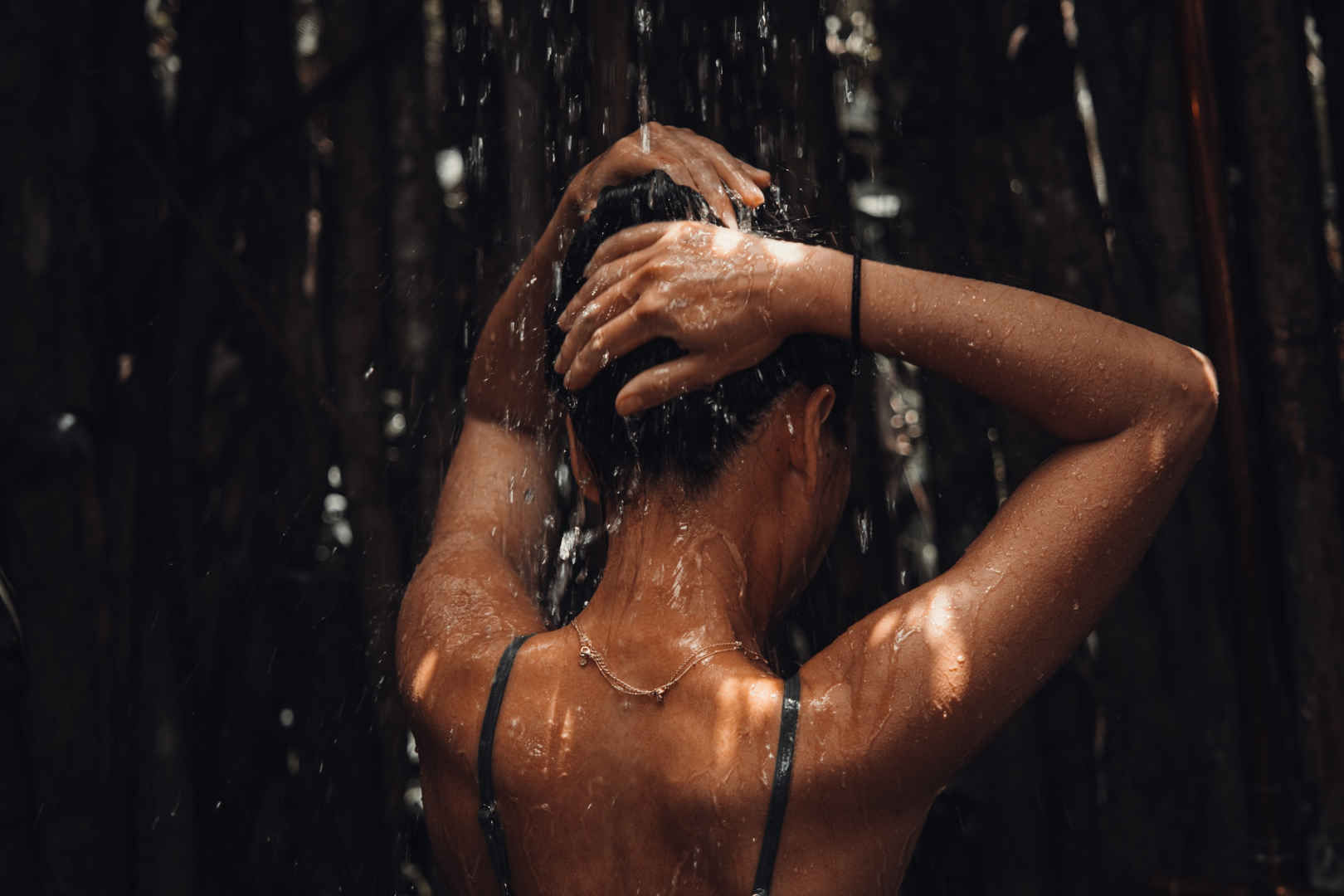 Woman washing hair in outdoor shower shot from behind