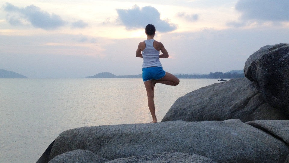 person doing yoga on a cliff side infront of ocean