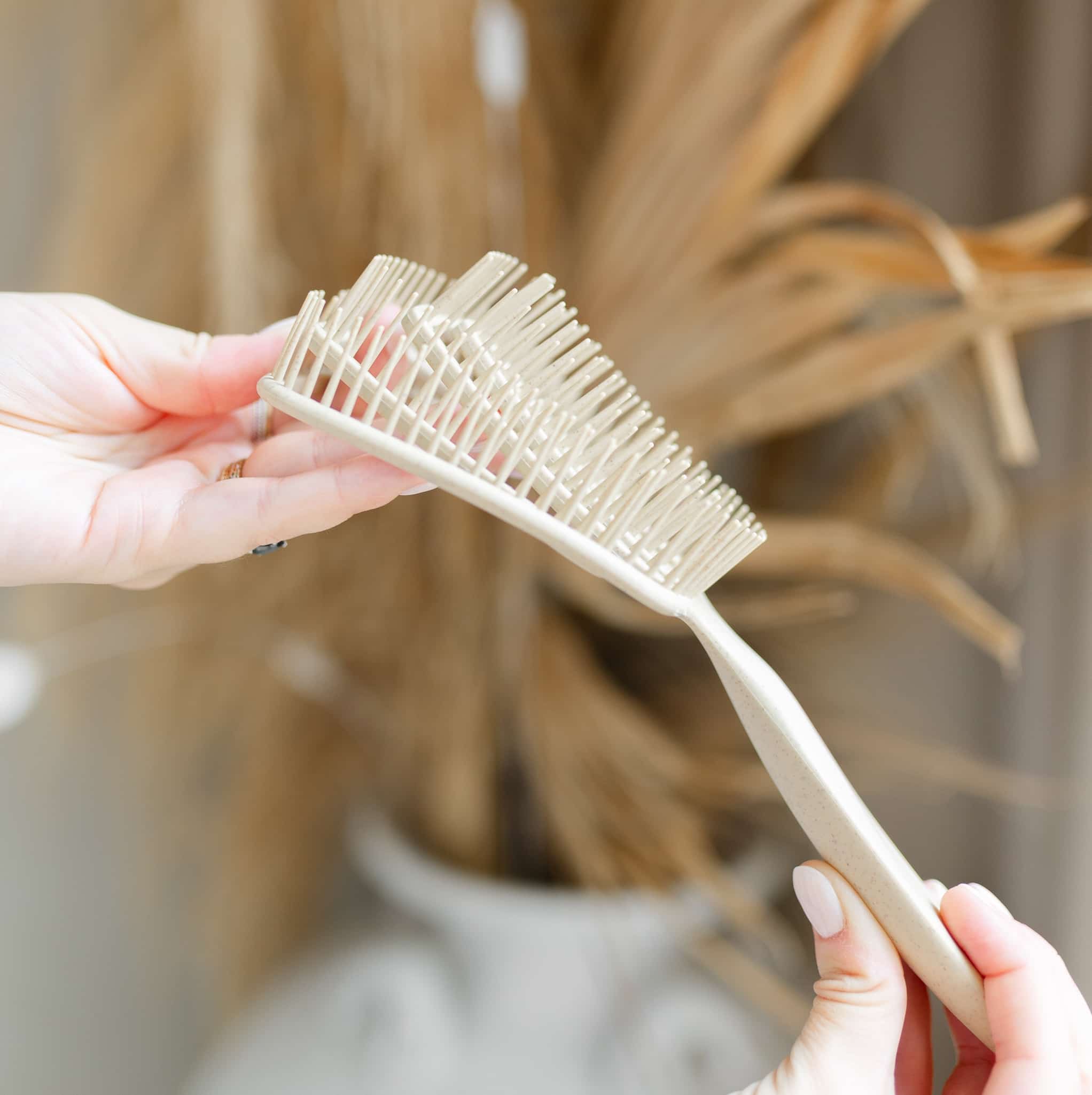 Unique 5-way flex design of TO112 Detangling Brush for pain-free detangling displayed in woman's hands. Made of heat-resistant, biodegradable wheat straw plastic.